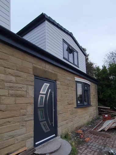 Contemporary dark grey front door with sleek silver handle and matching double glazing windows on a stone property.