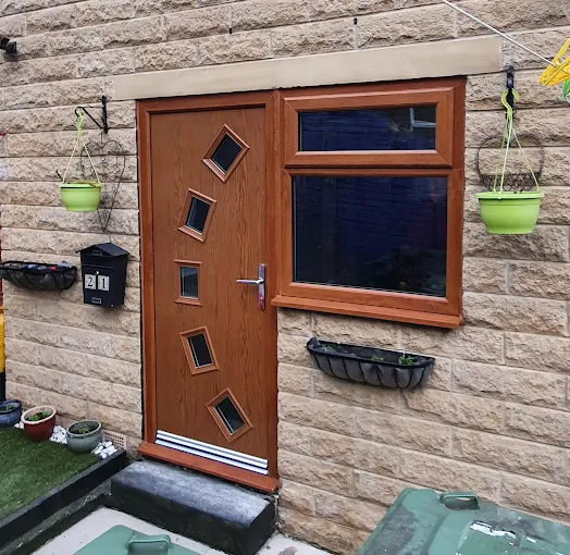 Light oak composite door with geometric glass panels alongside matching uPVC double glazing on a stone cottage wall.