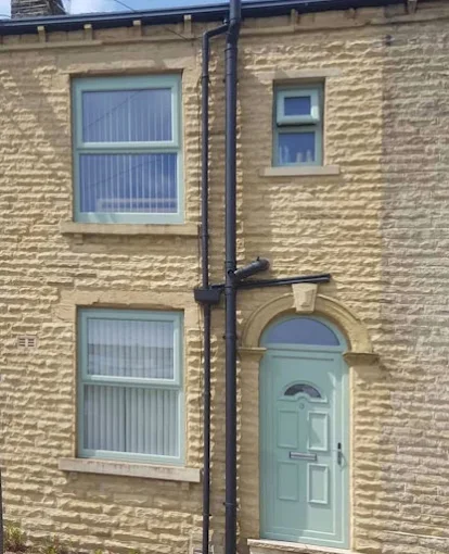 Sage green uPVC double glazing windows and matching front door on a traditional West Yorkshire stone house facade.